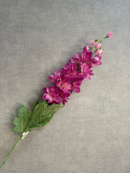 Roze kunstbloem Delphinium Cherise met volle bloei en lange steel, liggend op grijze achtergrond.