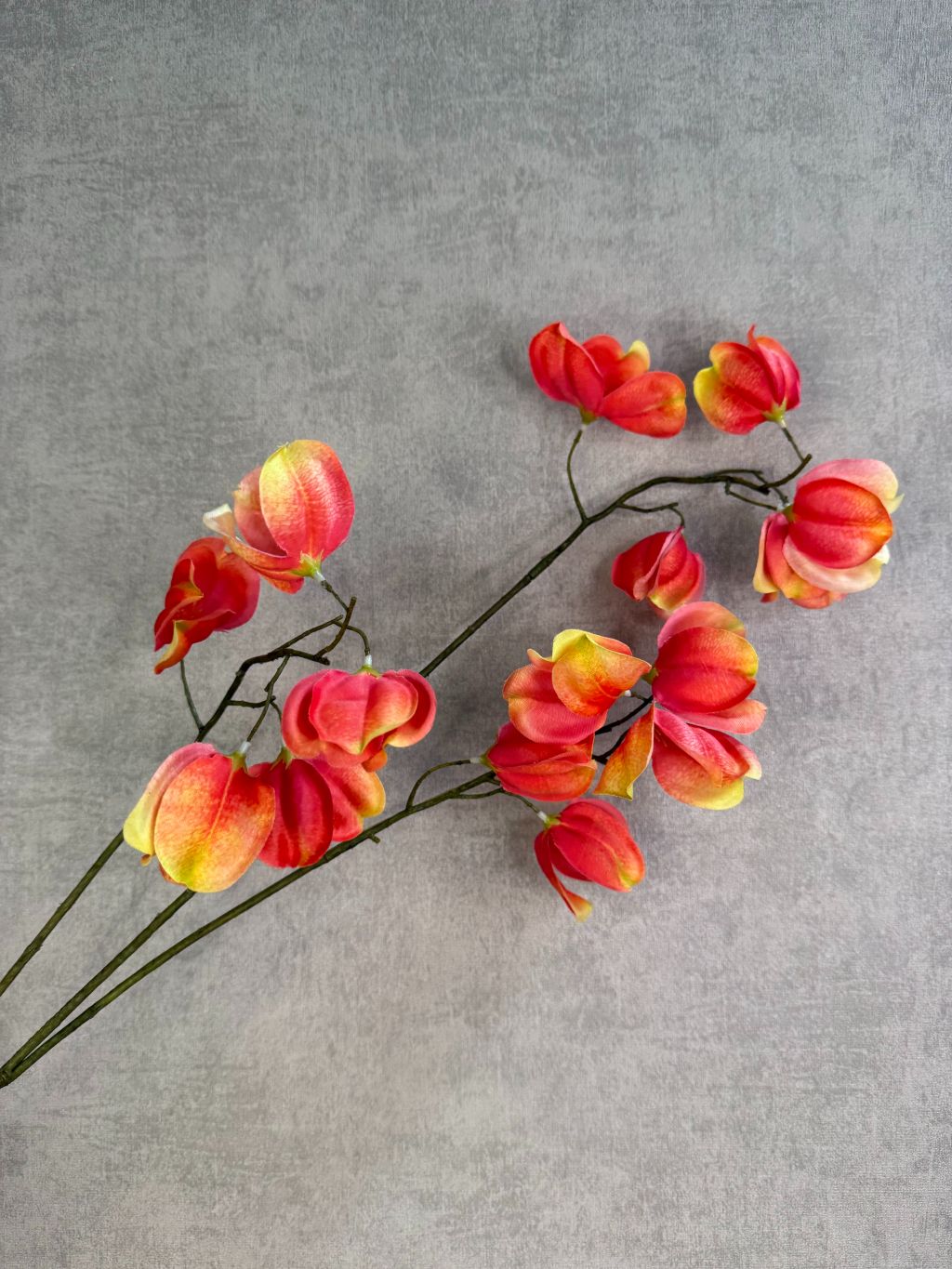 Kunstbloem Dipteronia met zalm-, oranje- en gele bloemblaadjes aan een lange groene steel tegen een neutrale achtergrond.