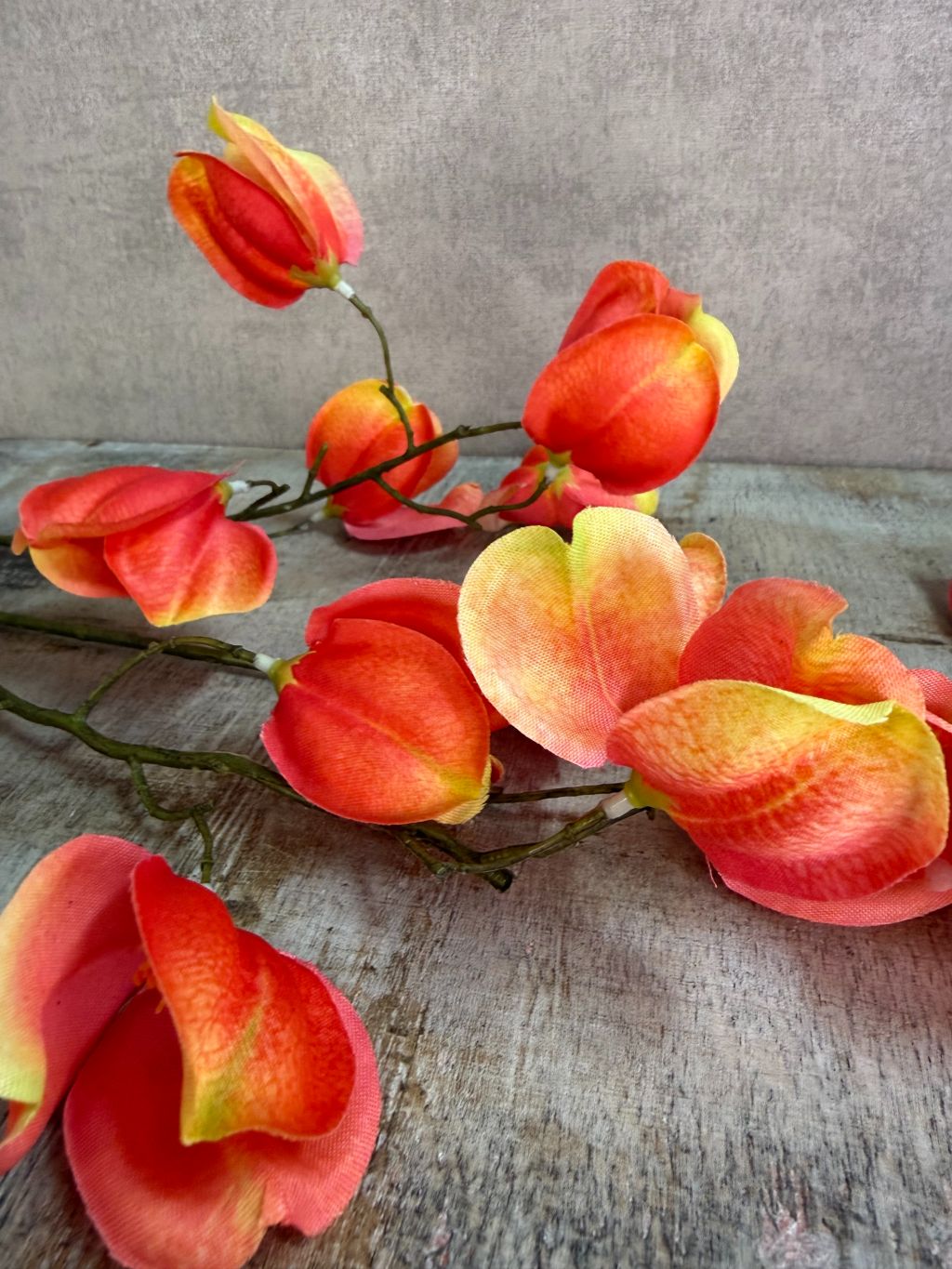 Kunstbloem Dipteronia met zalm-, oranje- en gele bloemblaadjes aan een lange groene steel tegen een neutrale achtergrond.