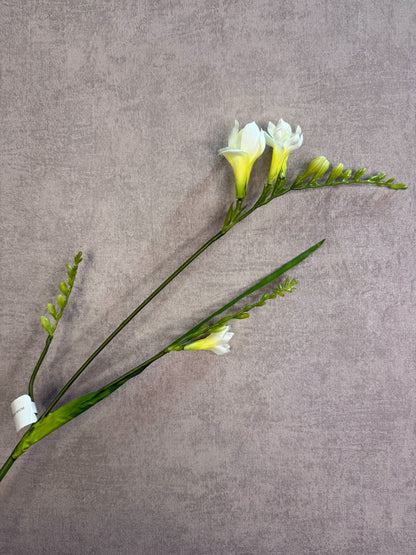 Witte kunstbloem freesia met slanke groene steel tegen een neutrale achtergrond.