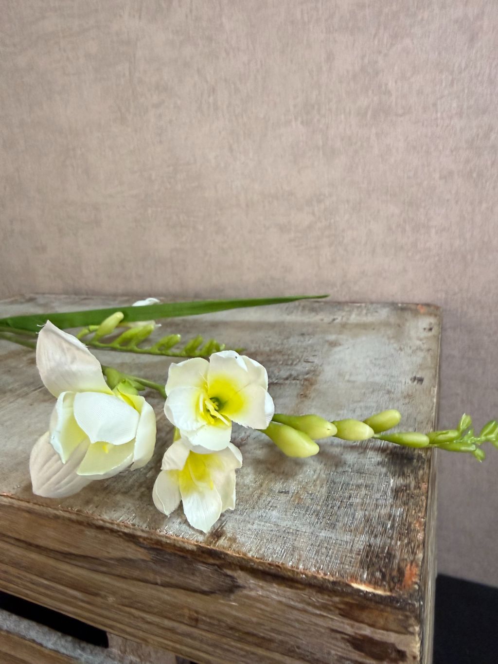 Witte kunstbloem freesia met slanke groene steel tegen een neutrale achtergrond.