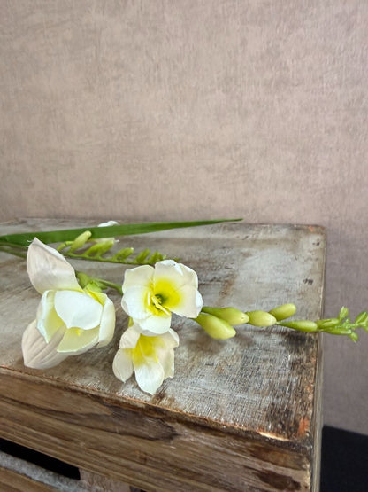 Witte kunstbloem freesia met slanke groene steel tegen een neutrale achtergrond.