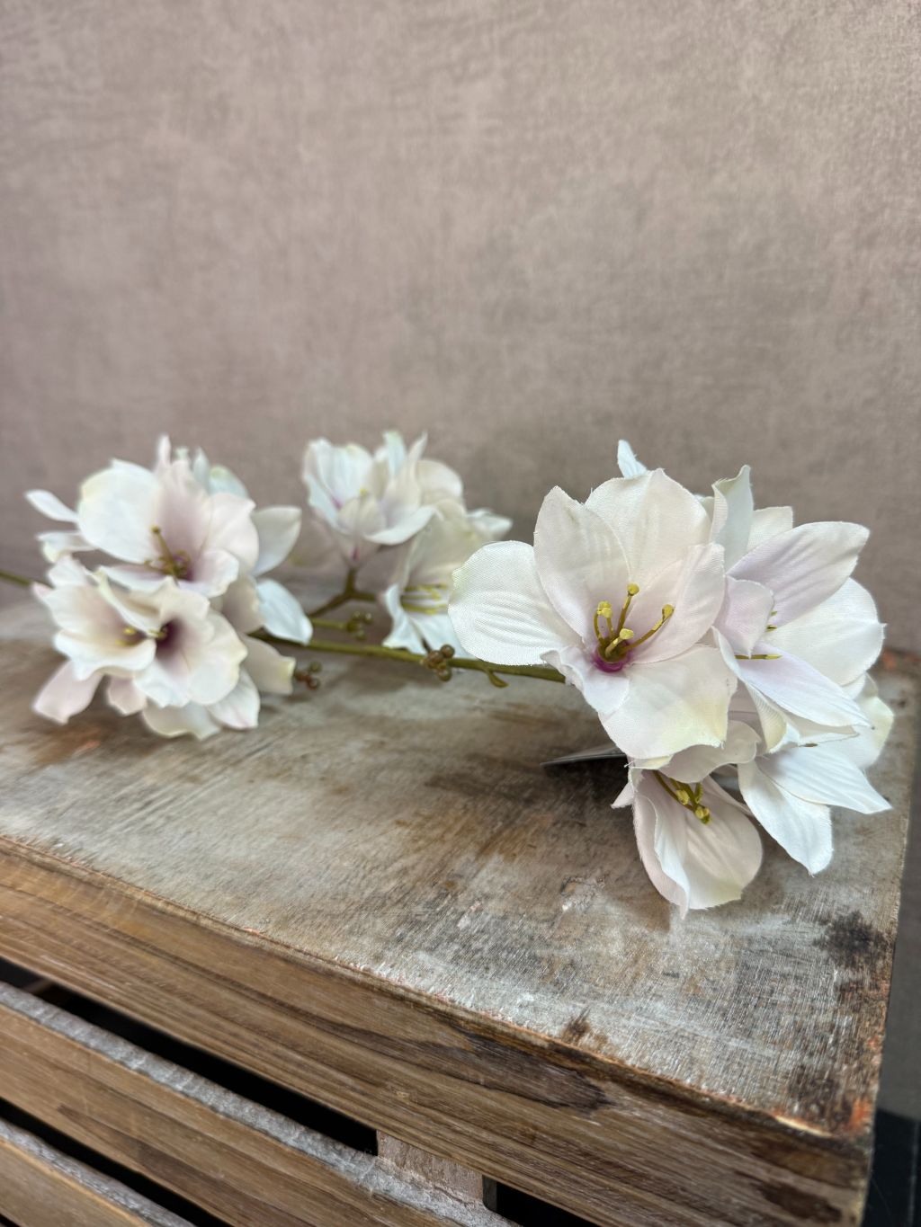 Kunstmatige hibiscus bloem in crème roze tinten met meerdere bloesems op een steel tegen een neutrale achtergrond.