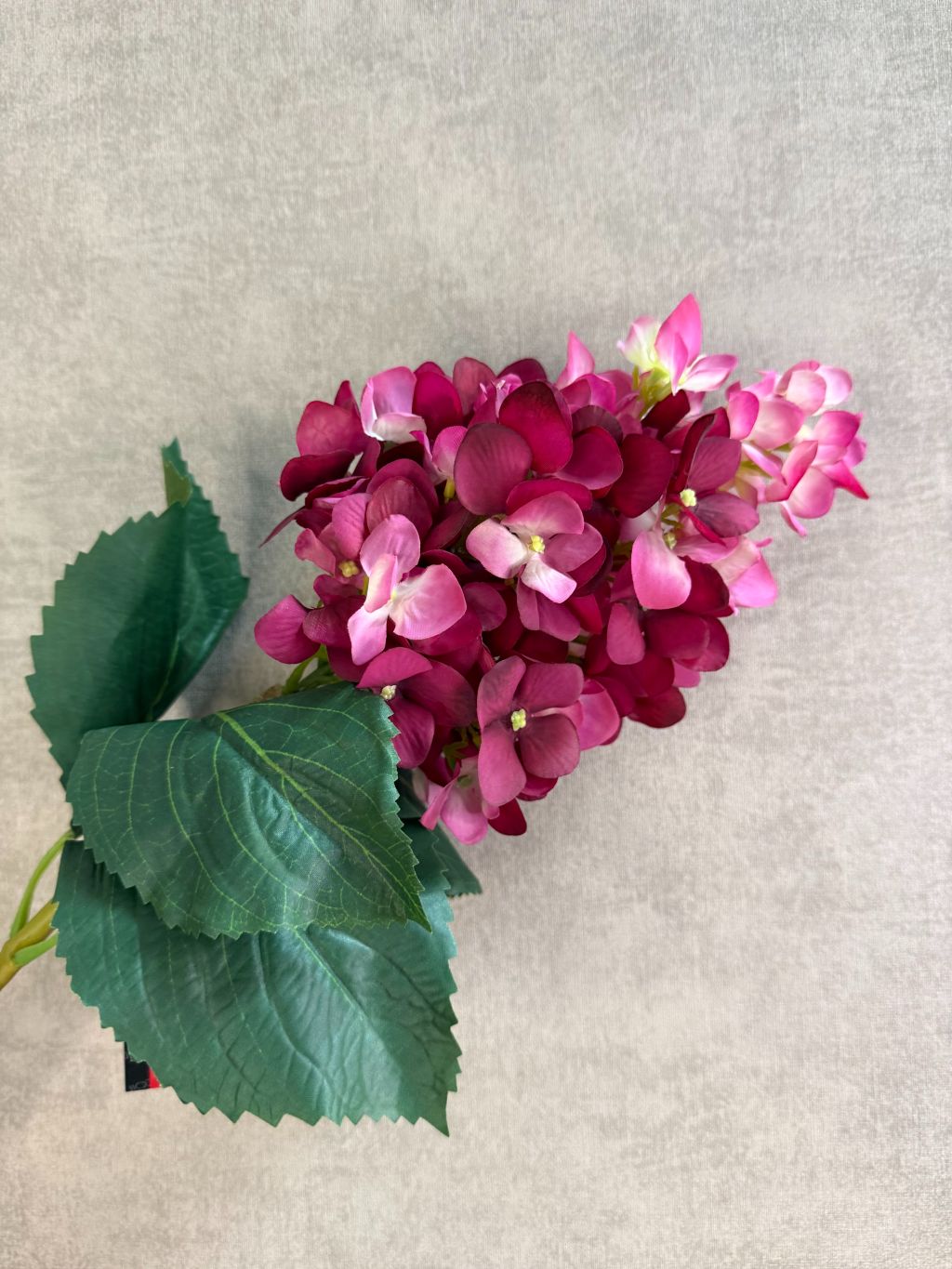 Kunstbloem hortensia in cherry red met volle bloemtros en roze-rode kleurschakering, liggend op een houten ondergrond.