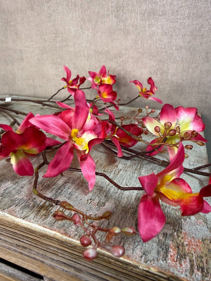 Roze kunstorchidee Cymbidium met meerdere bloemen en knoppen op lange steel, liggend op een houten ondergrond.