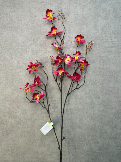 Roze kunstorchidee Cymbidium met meerdere bloemen en knoppen op lange steel, liggend op een houten ondergrond.