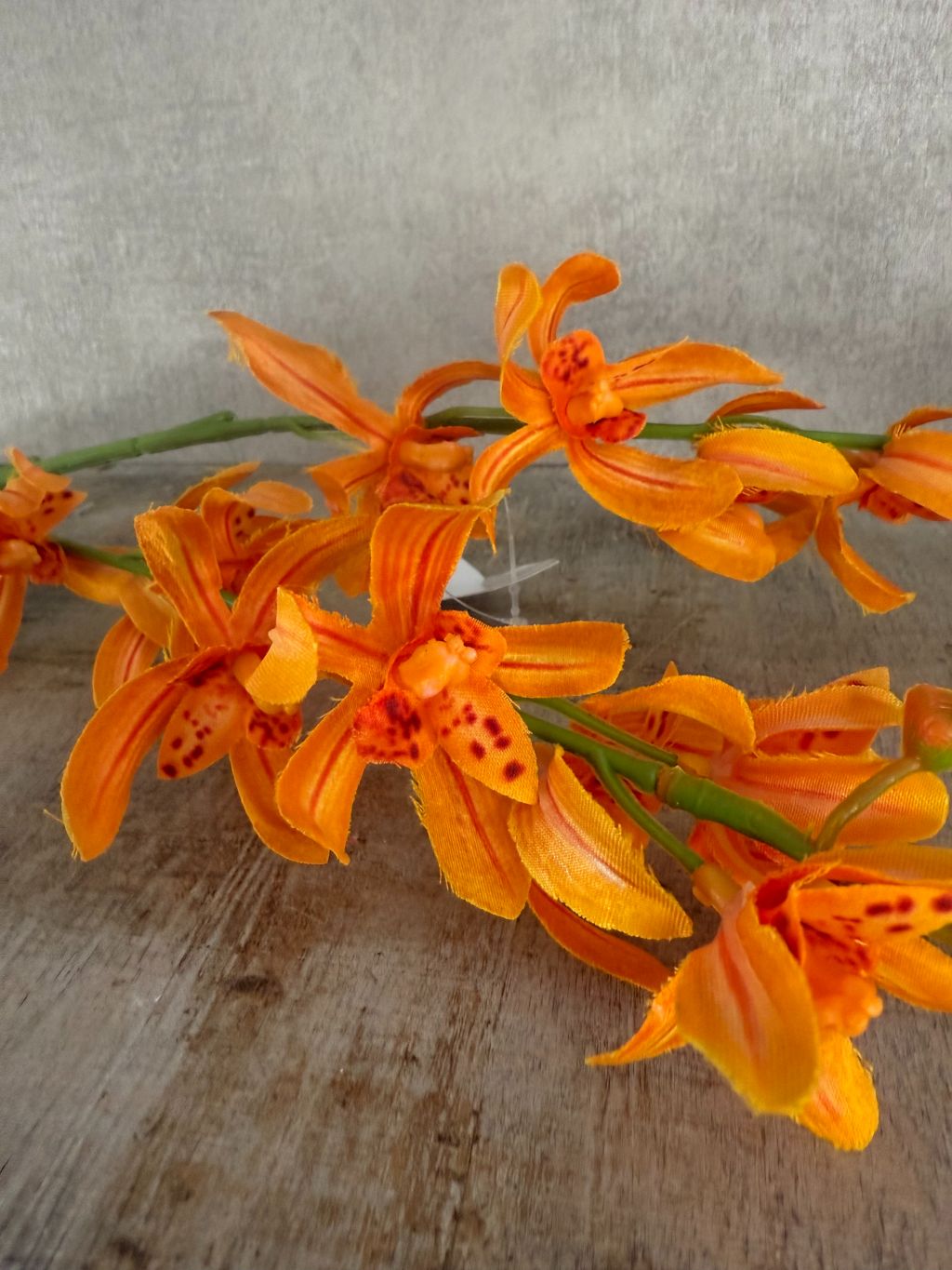Oranje kunstorchidee met lange steel en realistische bloemen tegen houten ondergrond