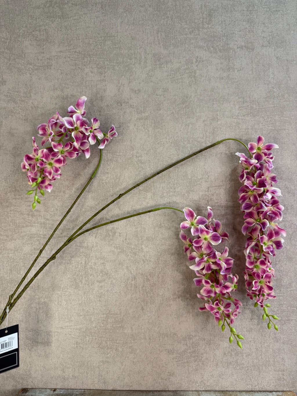 Paars roze kunstbloem Wisteria met hangende bloemtrossen en groene steel op een neutrale achtergrond.