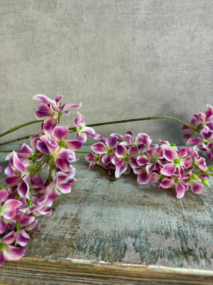 Paars roze kunstbloem Wisteria met hangende bloemtrossen en groene steel op een neutrale achtergrond.