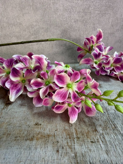 Paars roze kunstbloem Wisteria met hangende bloemtrossen en groene steel op een neutrale achtergrond.