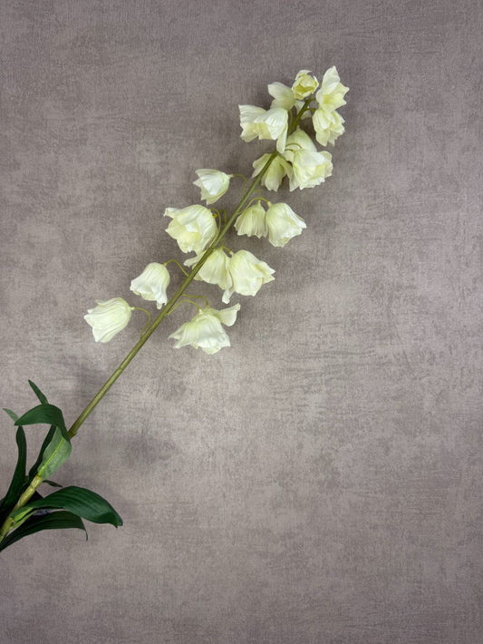 Crèmekleurige kunstbloem Campanula met klokvormige bloemen en groene bladeren tegen een neutrale achtergrond.