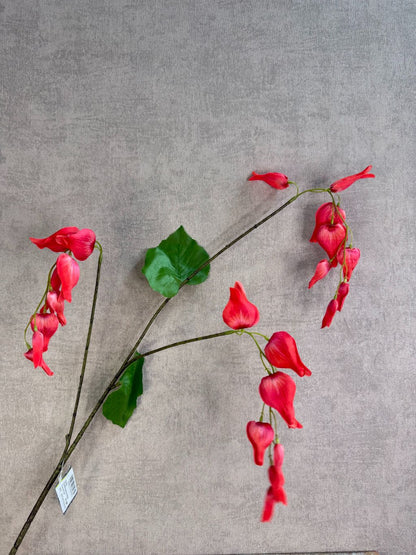 Rode kunstbloem Dicentra met hangende bloemen en groene bladeren, liggend op een neutrale achtergrond.