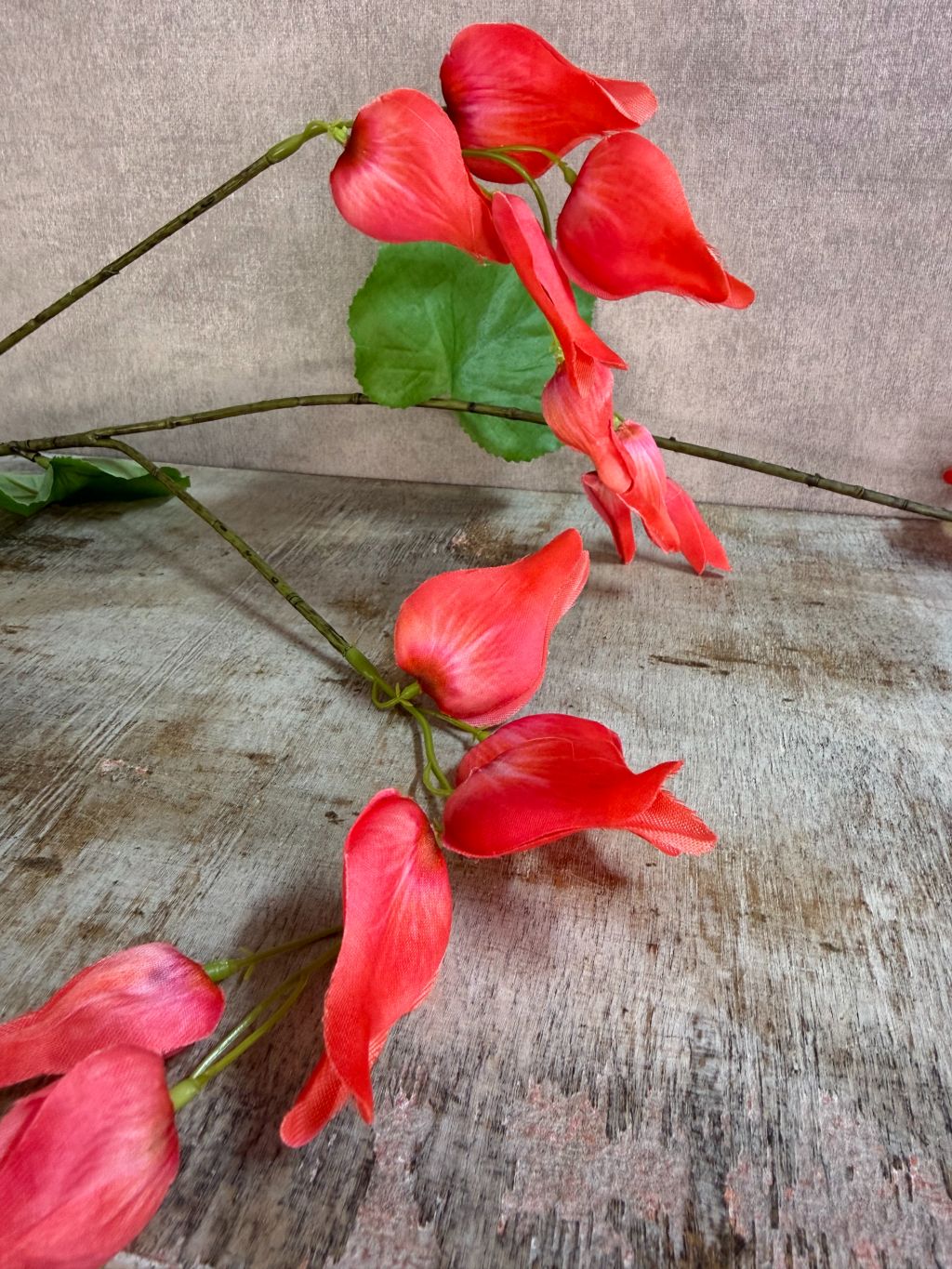 Rode kunstbloem Dicentra met hangende bloemen en groene bladeren, liggend op een neutrale achtergrond.