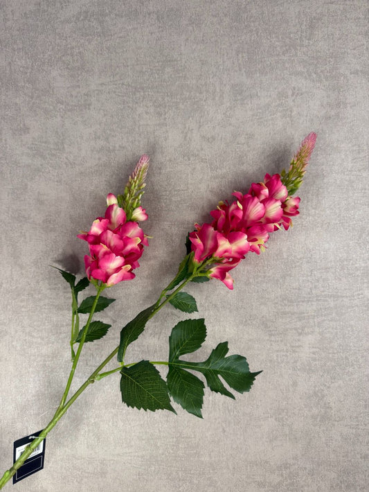 Kunstbloem lupine in fuchsia met groene bladeren en dubbele bloemtros, gefotografeerd tegen een neutrale grijze achtergrond.