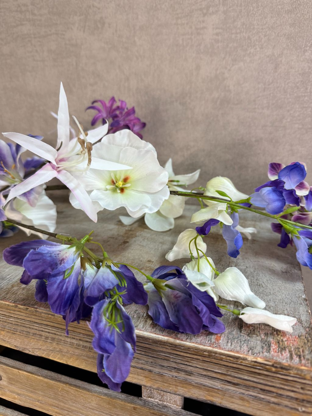 Extra lange kunstbloem met gemengde bloemen in wit, blauw en paars, liggend op een neutrale achtergrond.