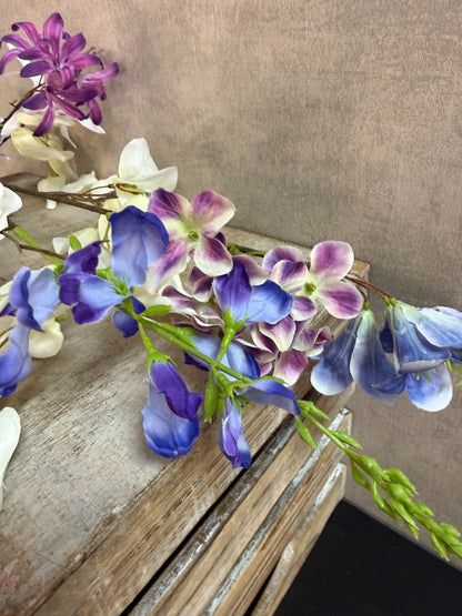 Extra lange kunstbloem met gemengde bloemen in wit, blauw en paars, liggend op een neutrale achtergrond.