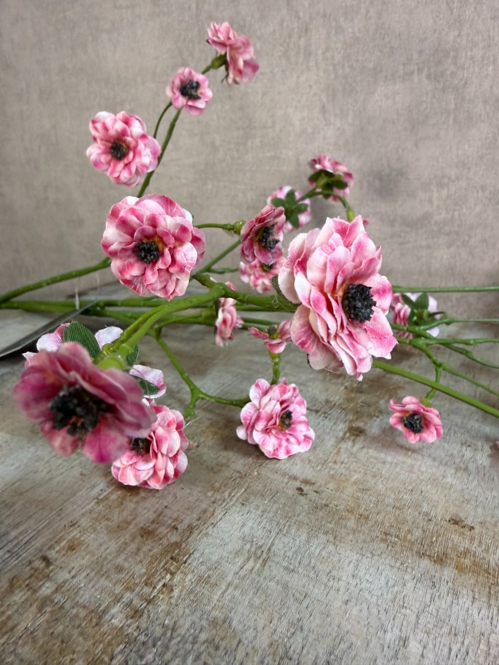 Kunstbloem mini roos in roze kleur met meerdere kleine bloemetjes aan een lange groene steel, gefotografeerd tegen een neutrale achtergrond.