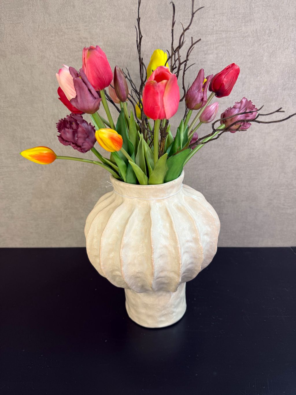 Kleurrijk kunstboeket met tulpen en decoratieve takken in een lichte vaas, vrolijke uitstraling en realistische afwerking.