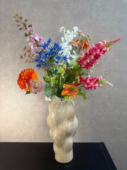 Kunstboeket met gemengde bloemen in diverse kleuren, geplaatst in een golvende beige vaas op zwarte ondergrond.