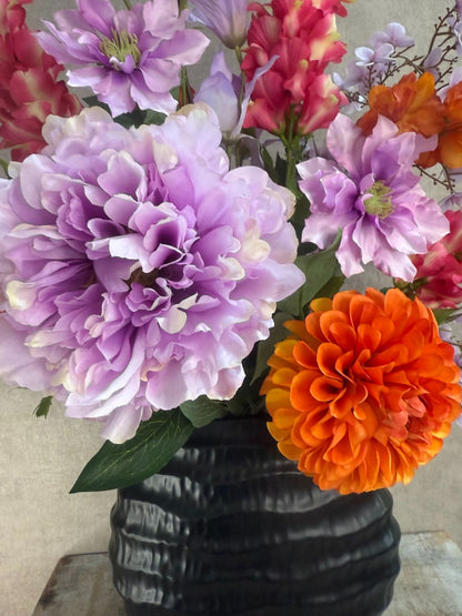 Kunstboeket in zwarte vaas met paarse, roze en oranje bloemen, front-facing geschikt voor vensterbank of wandmeubel.
