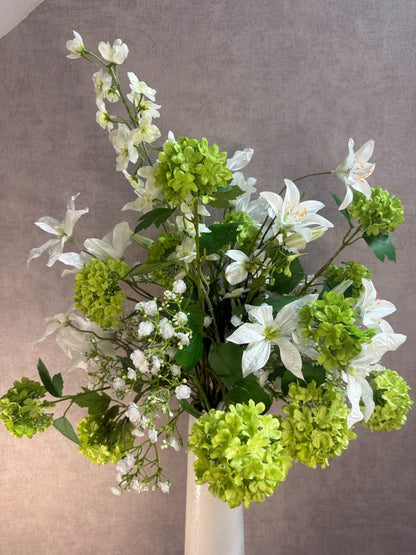 Kunstboeket met witte bloemen en groene sneeuwballen in een hoge crème vaas op zwarte ondergrond.