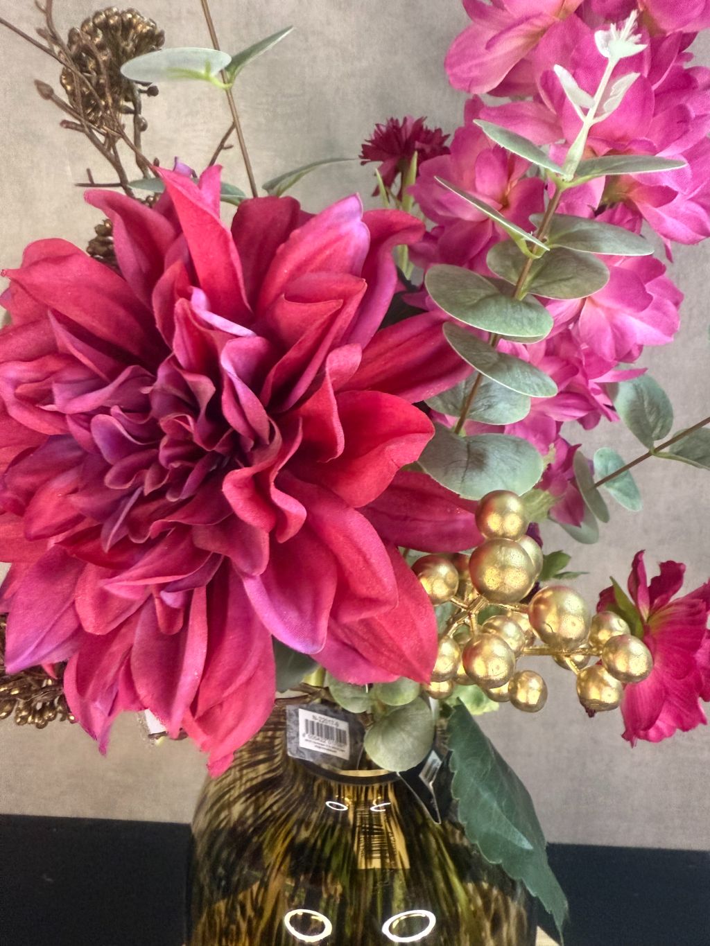 Kunstboeket met fuchsia pioenrozen, orchideeën en bordeaux bloemen in een glasvaas op houten ondergrond.