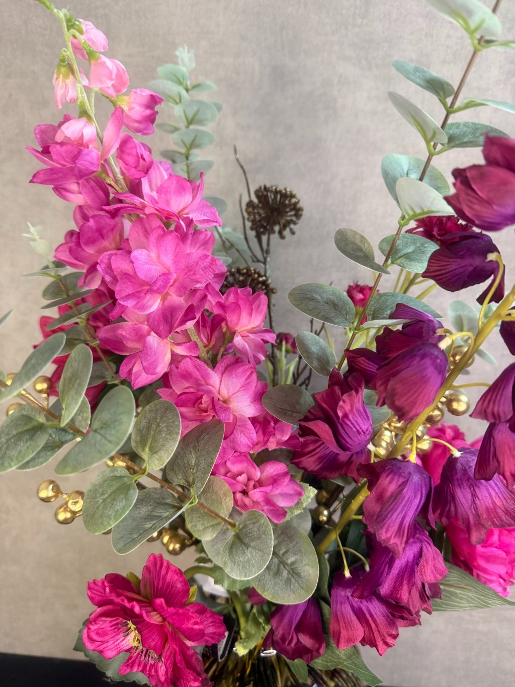 Kunstboeket met fuchsia pioenrozen, orchideeën en bordeaux bloemen in een glasvaas op houten ondergrond.