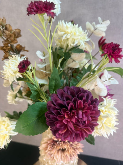 Kunstboeket Noëlle – volle bos kunstbloemen in beige, bruin en bordeaux tinten in een beige vaas tegen grijze achtergrond.