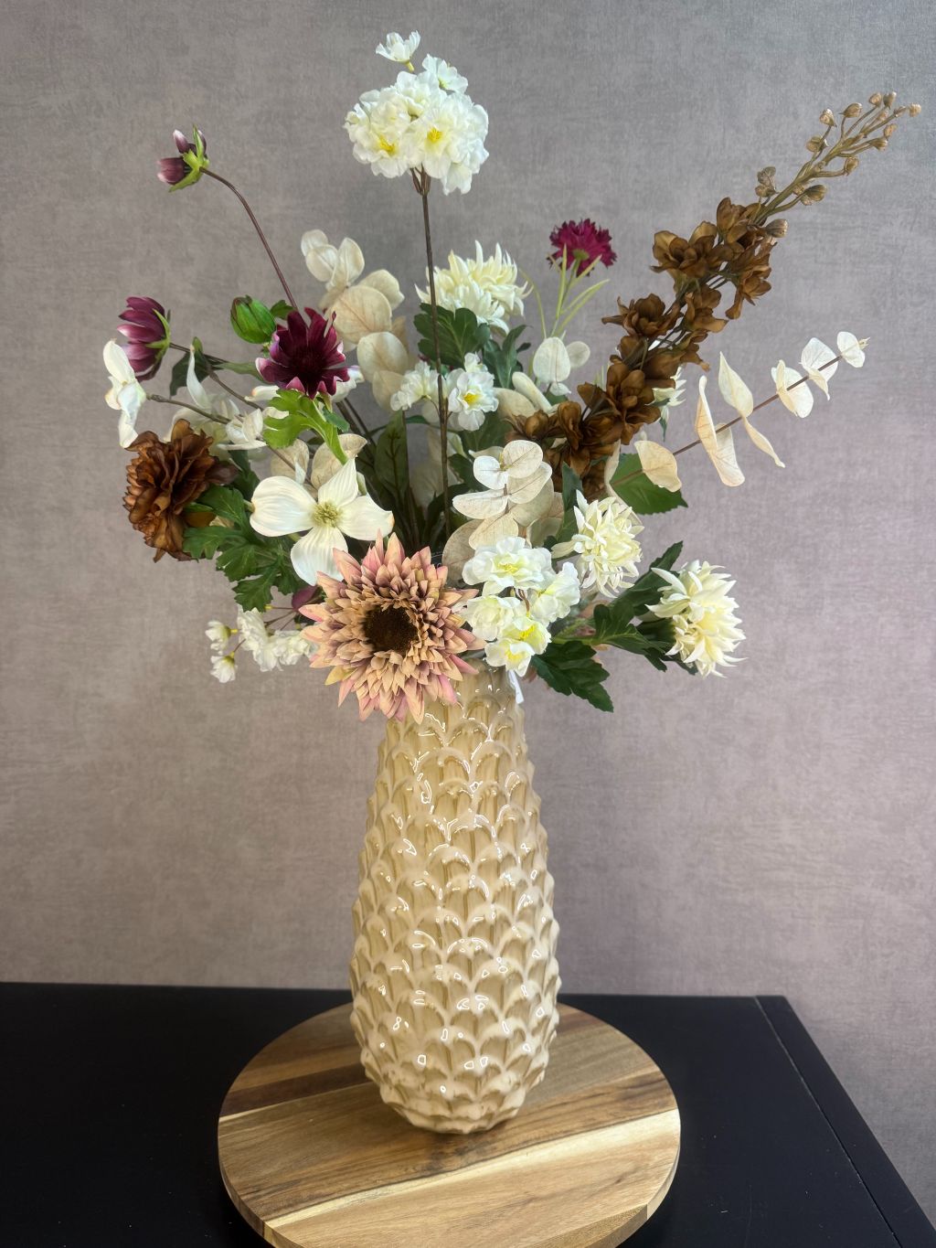 Kunstboeket Noëlle – volle bos kunstbloemen in beige, bruin en bordeaux tinten in een beige vaas tegen grijze achtergrond.