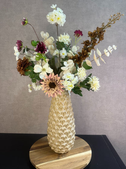 Kunstboeket Noëlle – volle bos kunstbloemen in beige, bruin en bordeaux tinten in een beige vaas tegen grijze achtergrond.