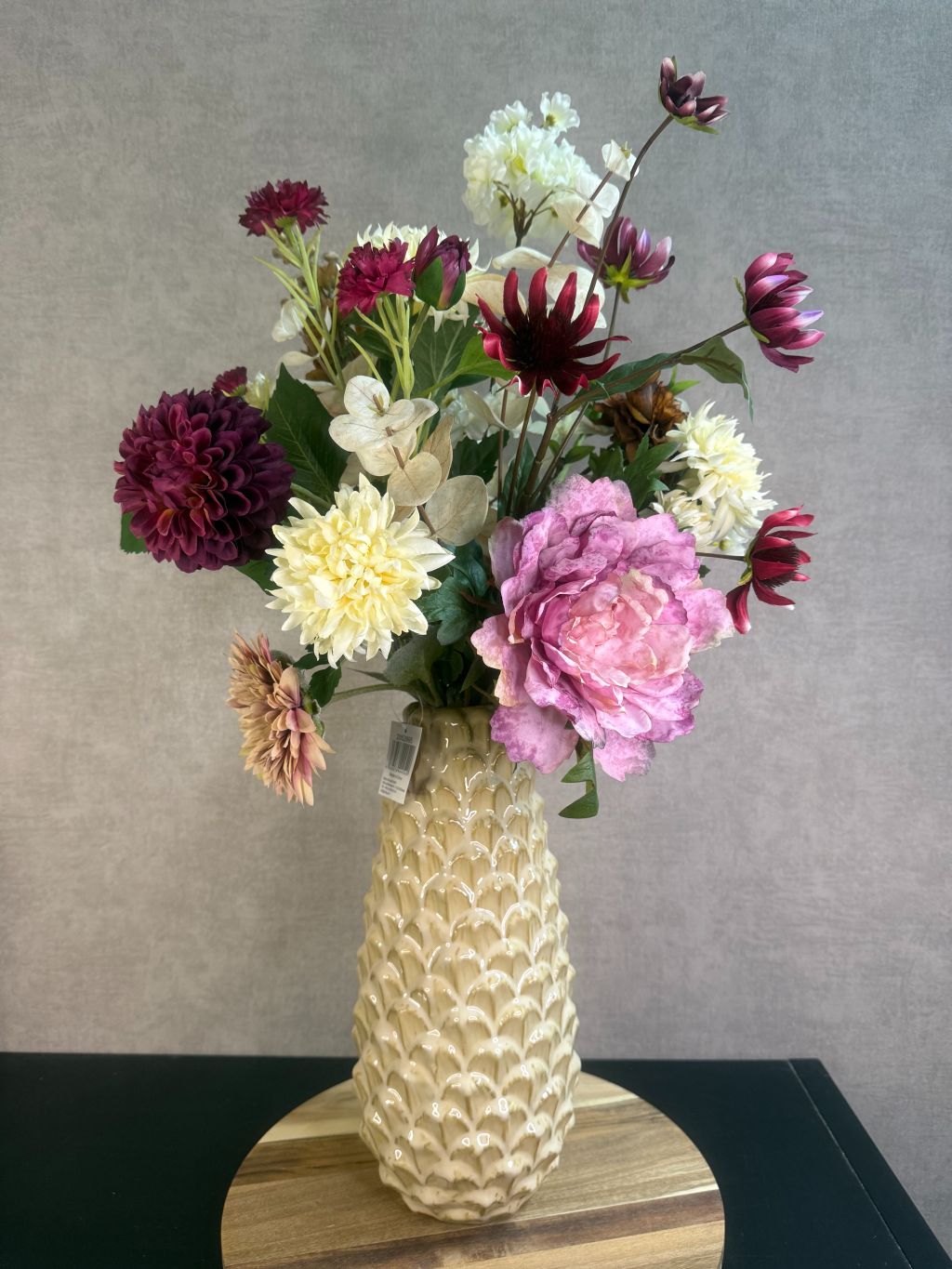 Kunstboeket Noëlle – volle bos kunstbloemen in beige, bruin en bordeaux tinten in een beige vaas tegen grijze achtergrond.