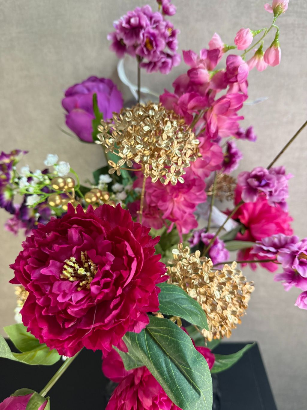 Luxe kunstboeket Novi met roze bloemen en goudaccenten in een zwarte vaas, stijlvol opgesteld tegen een neutrale achtergrond.