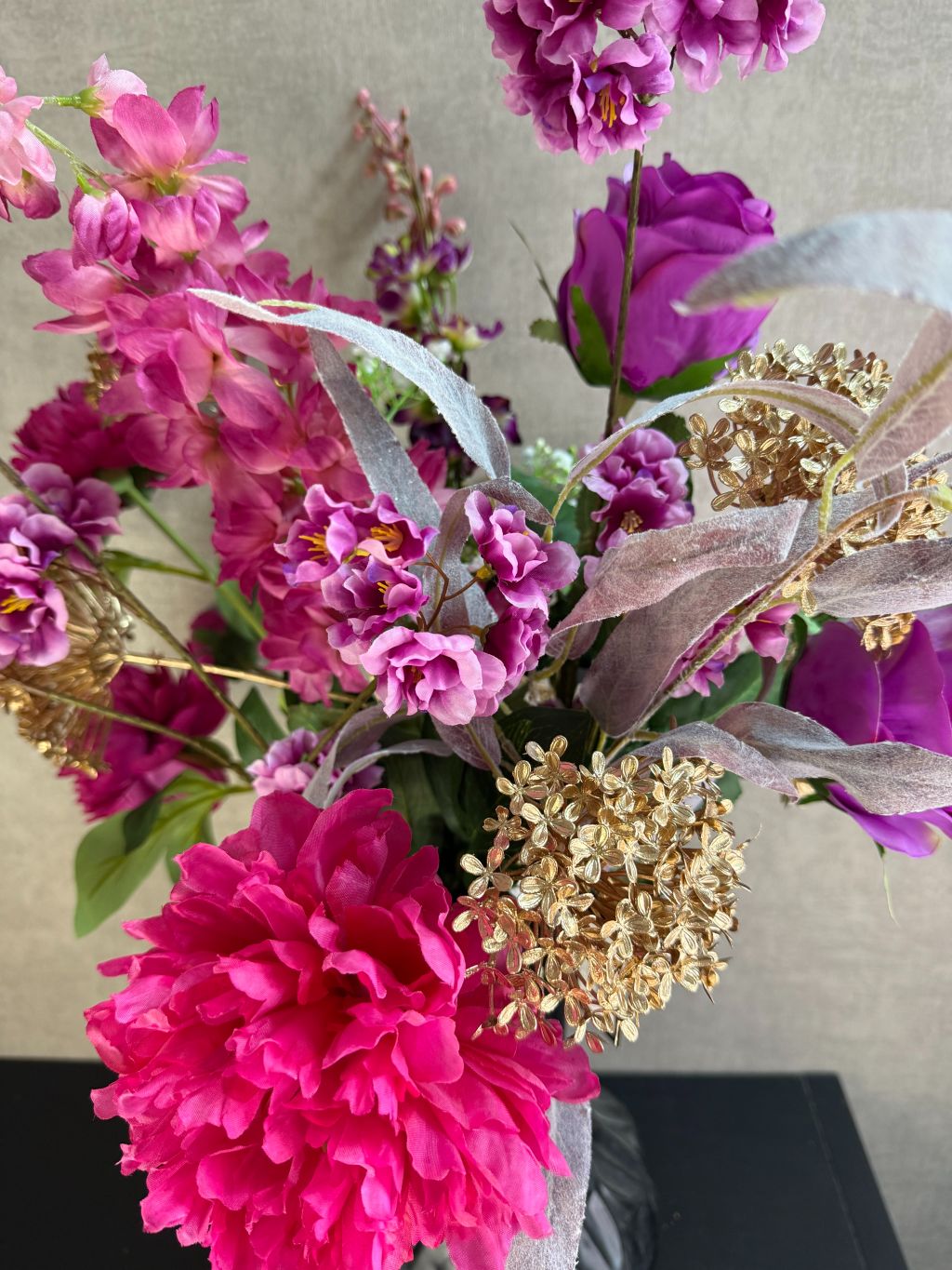 Luxe kunstboeket Novi met roze bloemen en goudaccenten in een zwarte vaas, stijlvol opgesteld tegen een neutrale achtergrond.