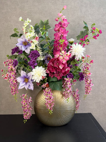 Groot kunstboeket Rosa in roze, paars en wit tinten met groene bladeren, geplaatst in een ronde goudkleurige vaas.