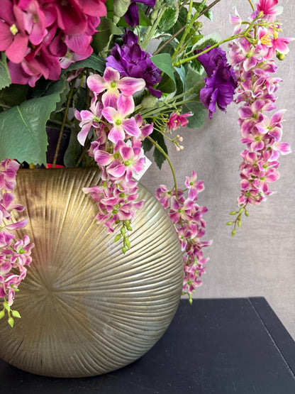 Groot kunstboeket Rosa in roze, paars en wit tinten met groene bladeren, geplaatst in een ronde goudkleurige vaas.