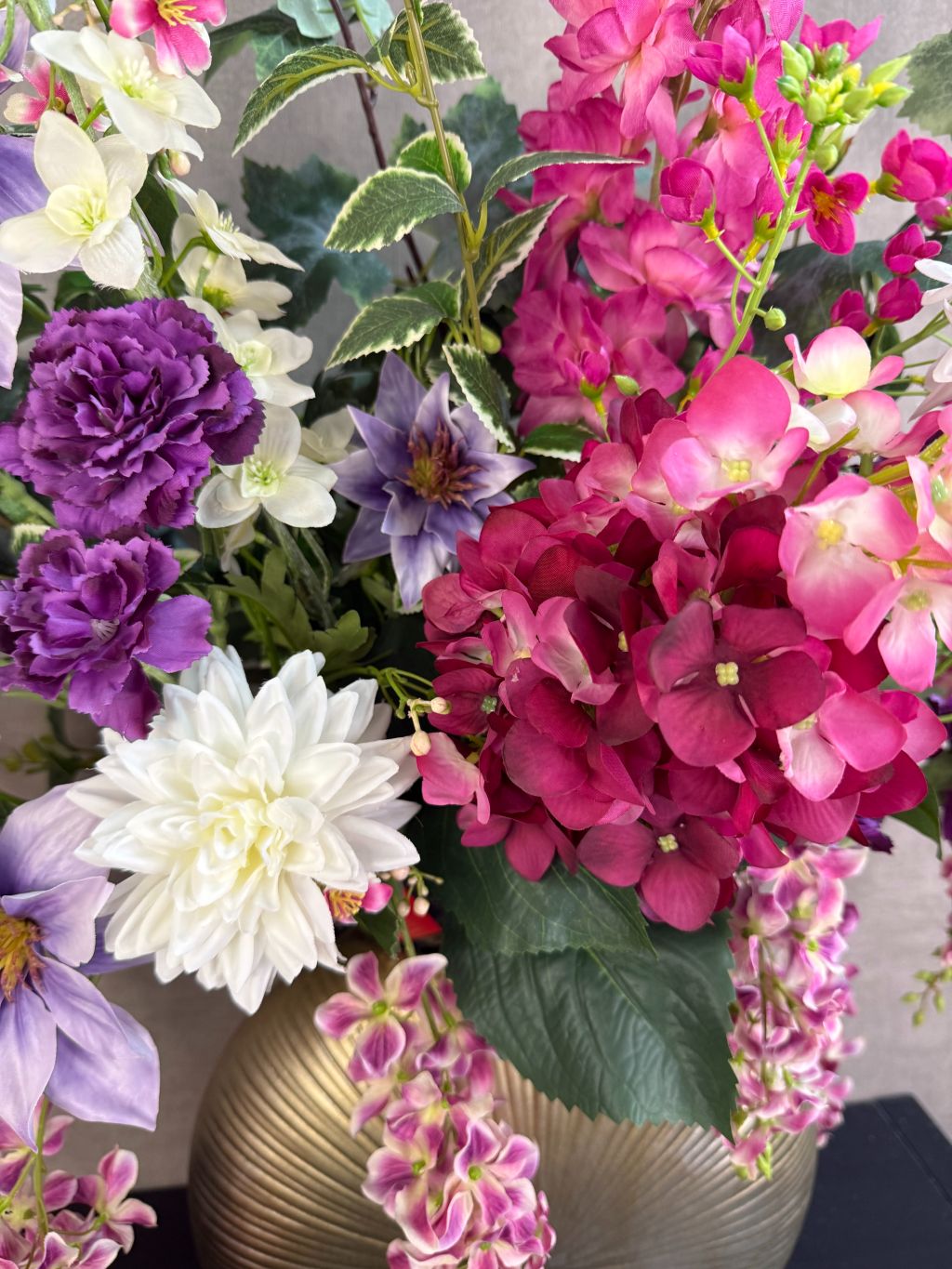 Groot kunstboeket Rosa in roze, paars en wit tinten met groene bladeren, geplaatst in een ronde goudkleurige vaas.