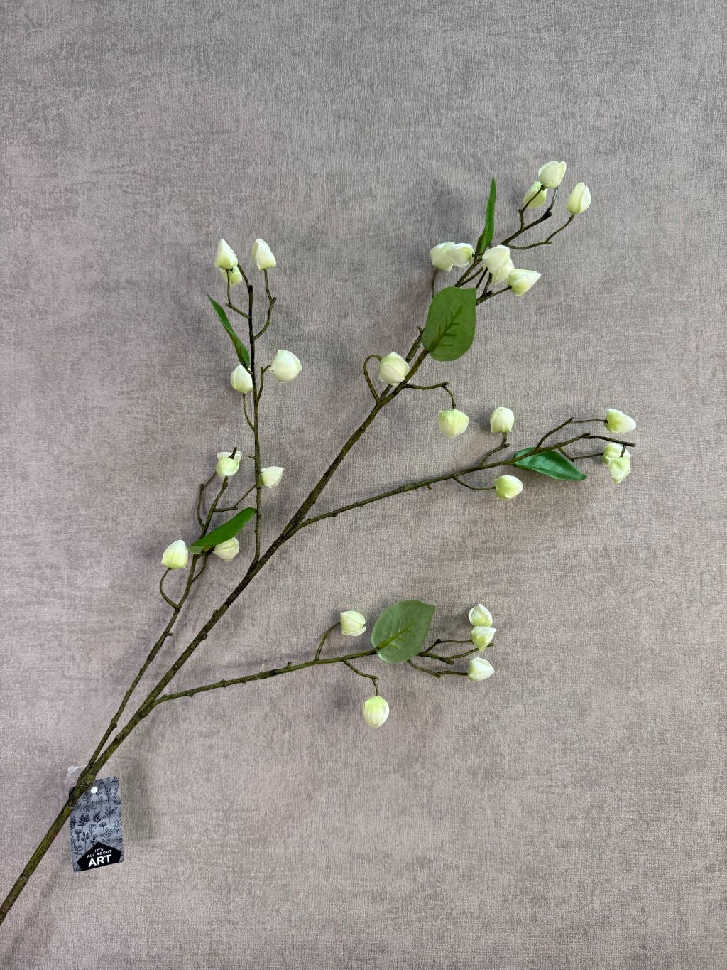 Kunsttak met crèmekleurige bloesemknoppen en groene bladeren liggend op een houten ondergrond.