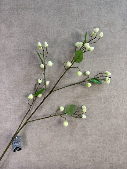 Kunsttak met crèmekleurige bloesemknoppen en groene bladeren liggend op een houten ondergrond.