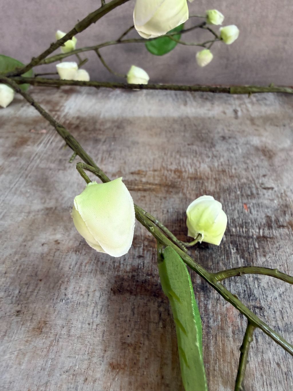 Kunsttak met crèmekleurige bloesemknoppen en groene bladeren liggend op een houten ondergrond.