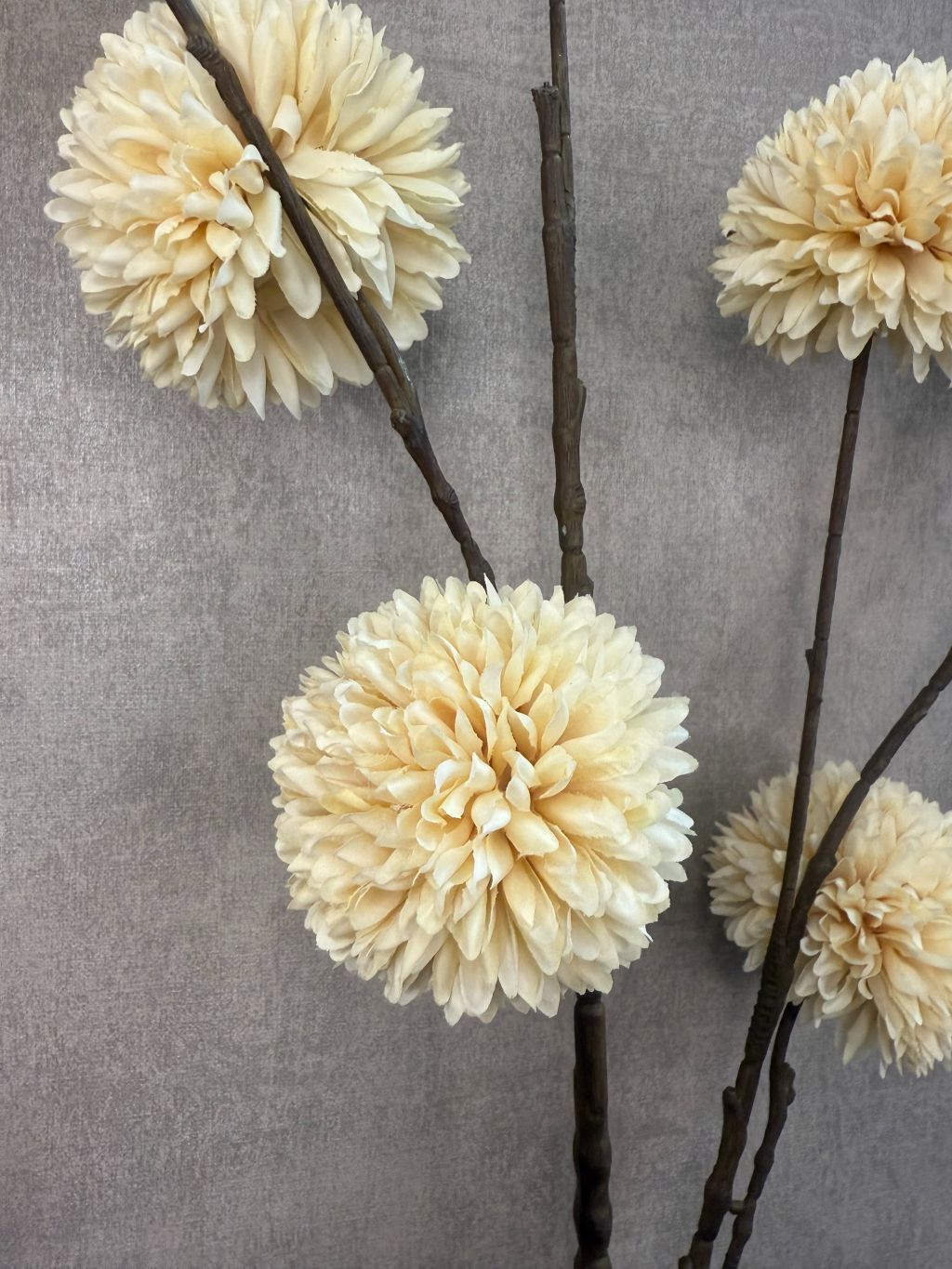 Crèmekleurige kunsttak met meerdere pompomvormige bloemen op donkere steel, tegen een neutrale achtergrond.