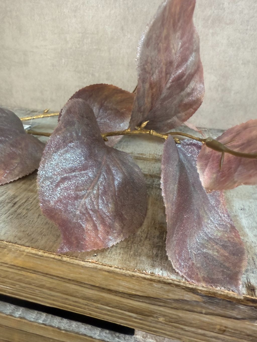 Kunsttak met bruine glanzende rozenbladeren op goudkleurige steel tegen grijze achtergrond.