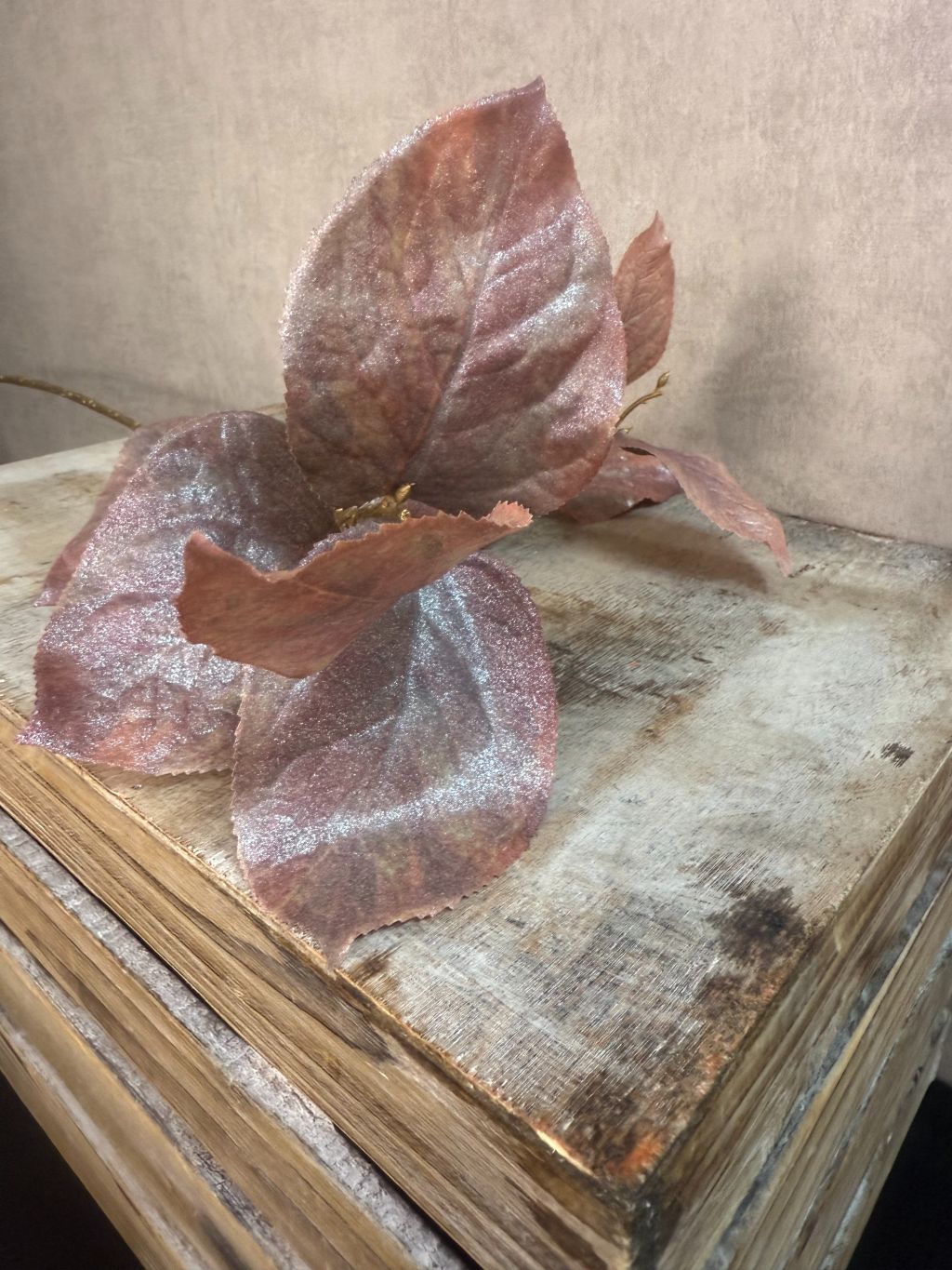 Kunsttak met bruine glanzende rozenbladeren op goudkleurige steel tegen grijze achtergrond.