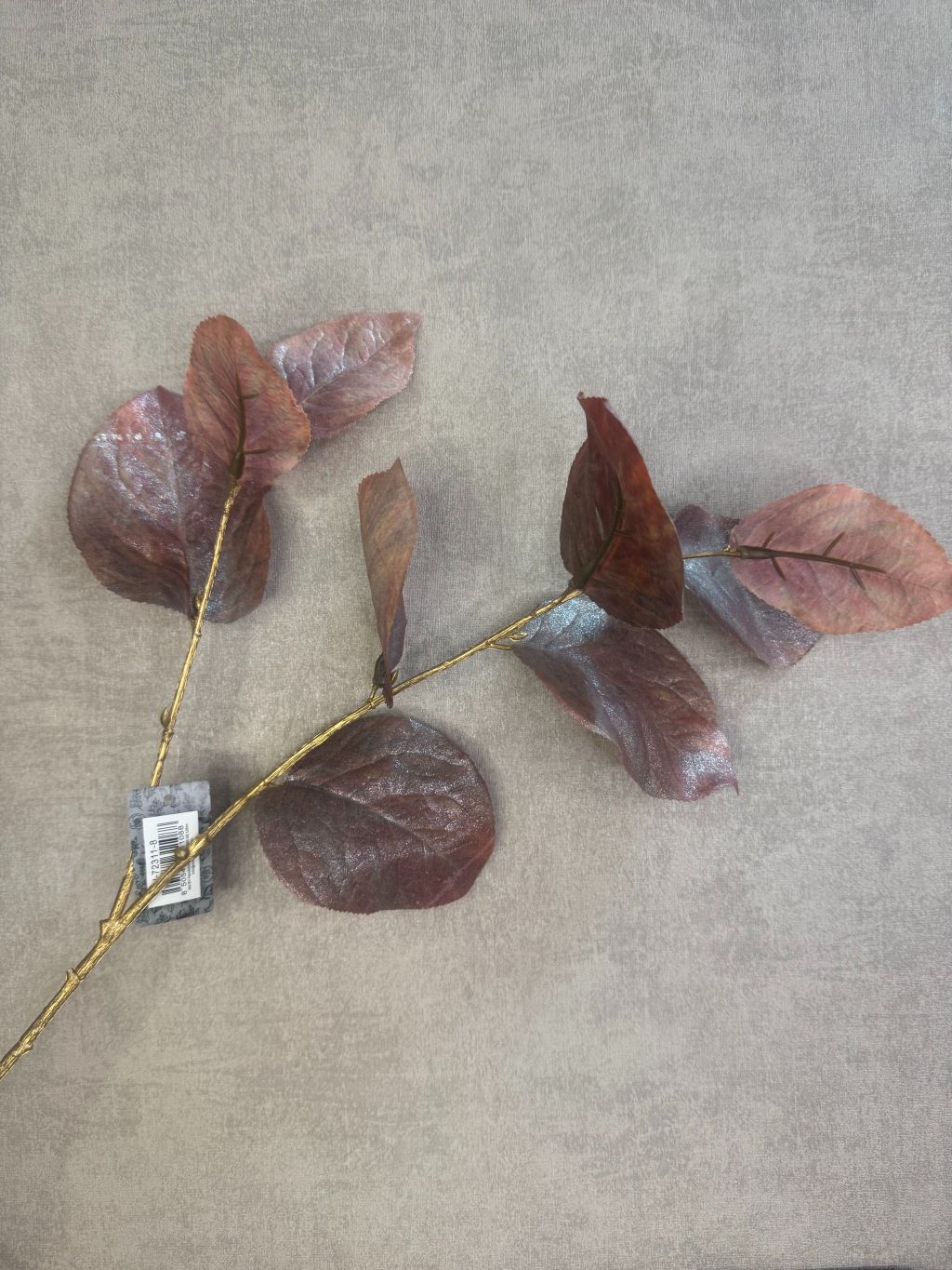 Kunsttak met bruine glanzende rozenbladeren op goudkleurige steel tegen grijze achtergrond.