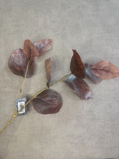 Kunsttak met bruine glanzende rozenbladeren op goudkleurige steel tegen grijze achtergrond.