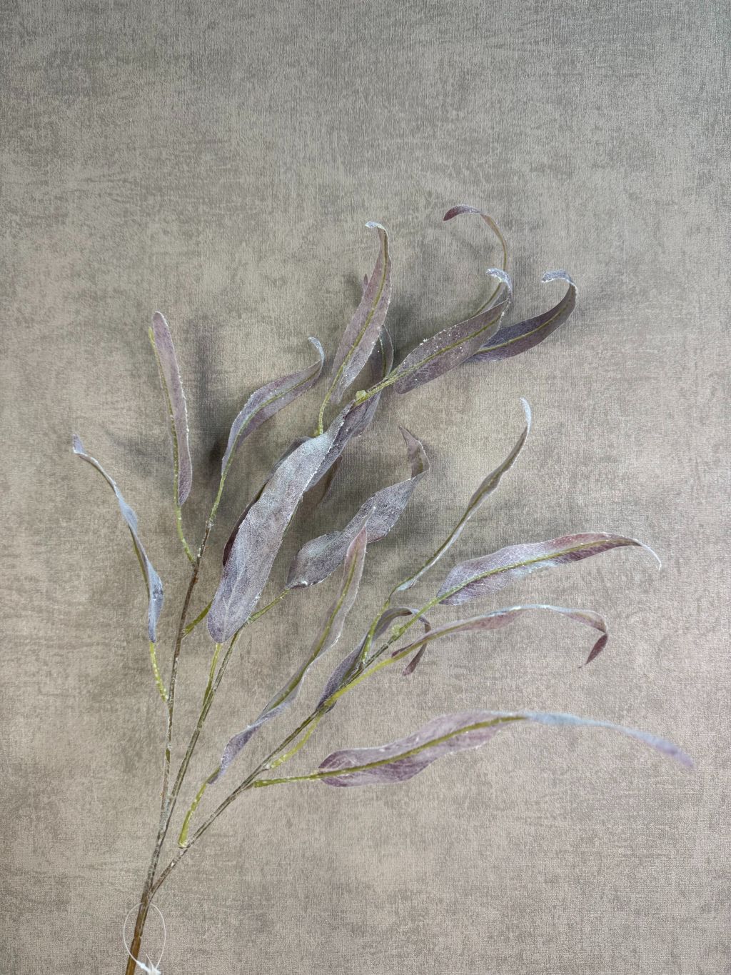 Paarse kunsttak eucalyptus met slanke bladeren en subtiele glitter tegen een neutrale achtergrond.