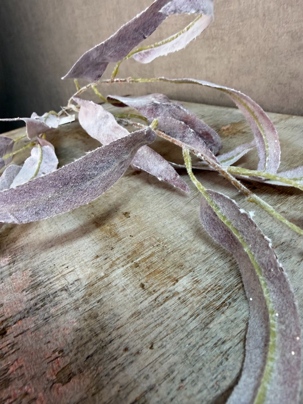 Paarse kunsttak eucalyptus met slanke bladeren en subtiele glitter tegen een neutrale achtergrond.