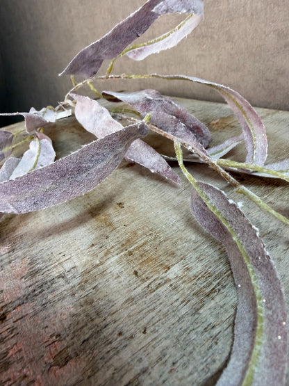 Paarse kunsttak eucalyptus met slanke bladeren en subtiele glitter tegen een neutrale achtergrond.