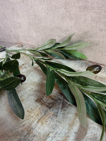 Groene kunsttak met olijfvruchten en langwerpige bladeren tegen een neutrale achtergrond.