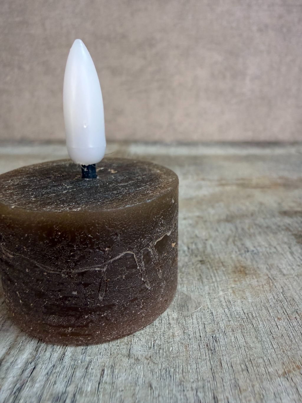 bruine led waxinelichtje met witte vlam op een houten ondergrond.