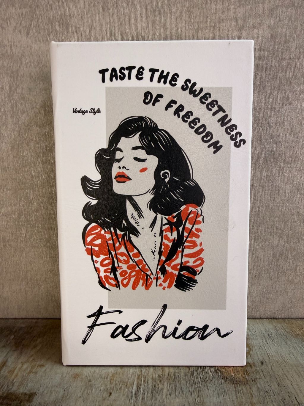 Wit opbergboek Fashion met illustratie en tekst op de voorkant, staand op een houten ondergrond.